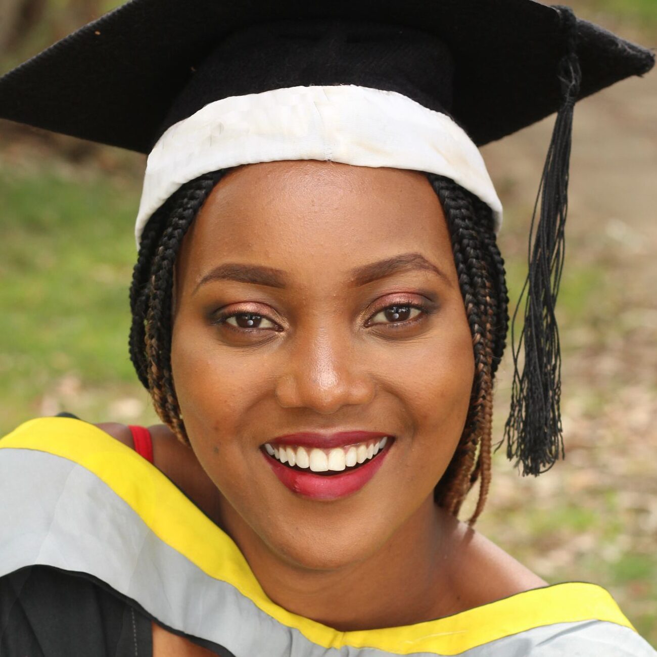 A smiling African American woman in graduation attire celebrates her achievement outdoors.